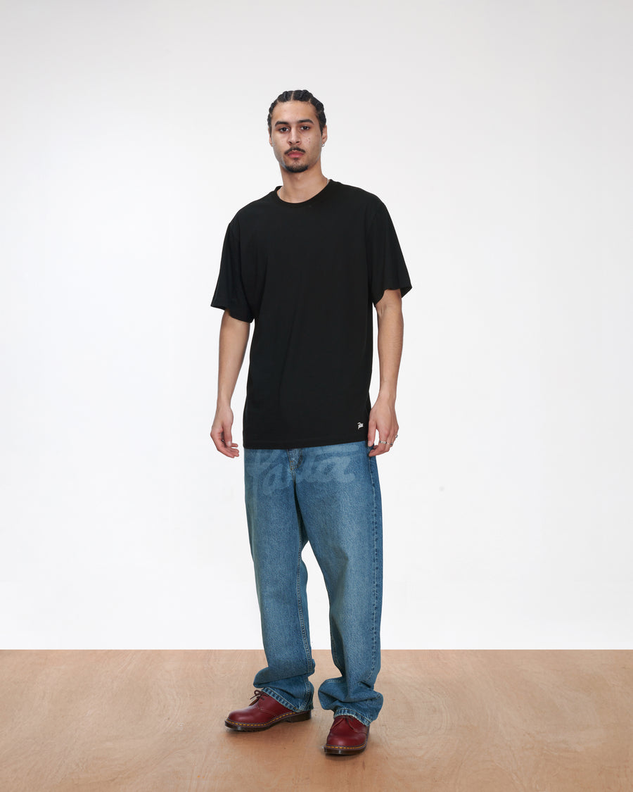 Model wearing a black Patta Tubular T-Shirt with relaxed blue jeans on a white backdrop.